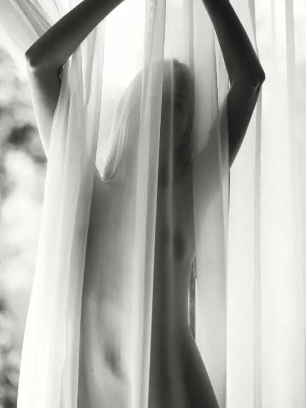 Intimate fine art portrait of a veiled woman in soft light, revealing desire, vulnerability, and sensual contrast in black and white