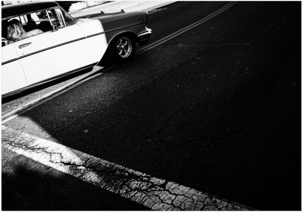 Black and white photograph of a classic white American car from the 1950s on a Venice Beach street, dynamic diagonal composition